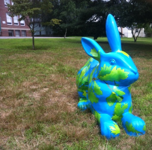 Avery Oak sits on a lawn. The blue bunny is covered with a network of oak tree branches, leaves, and acorns. 