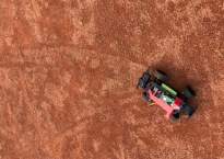 View of a remote control car from above, showing the tracks the car's tires have left on the bright orange dirt of a baseball field.