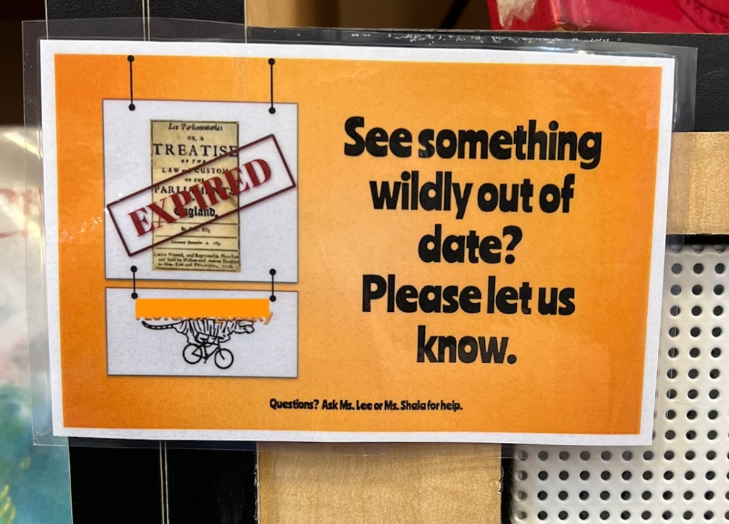 Orange sign that says: "See something wildly out of date? Please let us know." The graphic on it shows a treatise written on parchment with "EXPIRED" stamped across it. 