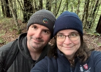 Image shows two smiling people paused for a selfie in a wooded area. My husband is wearing a knit winter cap with a Google logo on it. I'm wearing a Beth Israel Deaconness Medical Center fleece jacket that Michael got while he was practicing at Beth Israel.